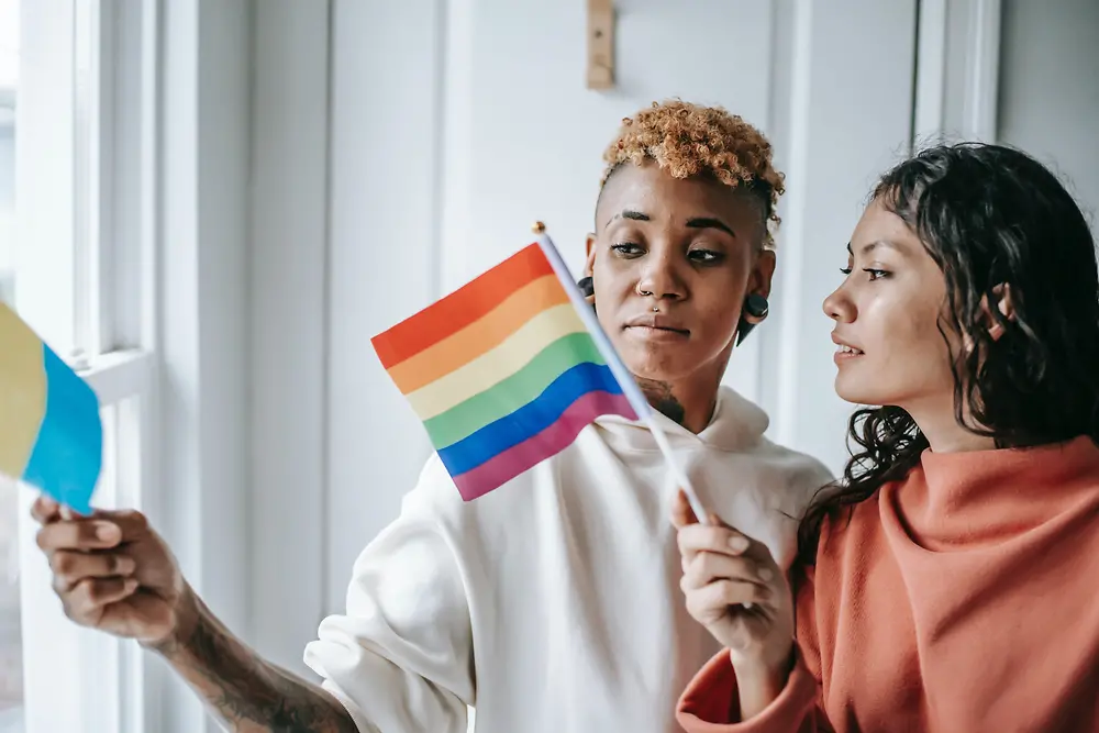 Két nő beszélget egymással, miközben egy LMBTQ+ zászlót tartanak a kezükben.