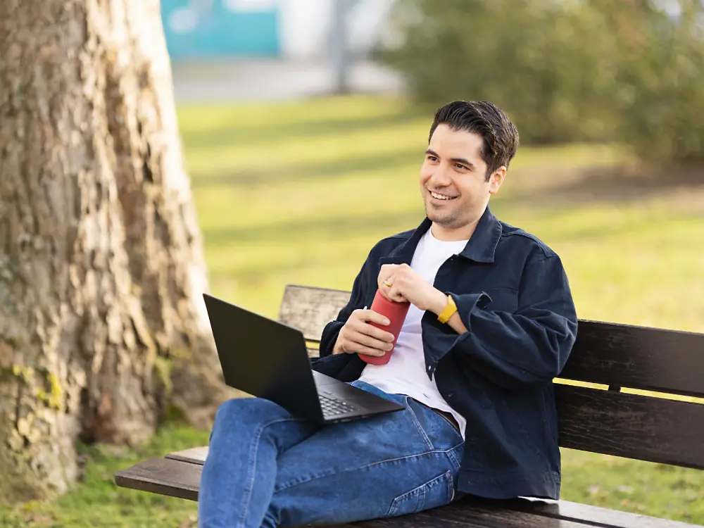 A Henkel egyik alkalmazottja egy padon ül egy parkban, és a laptopján dolgozik. 