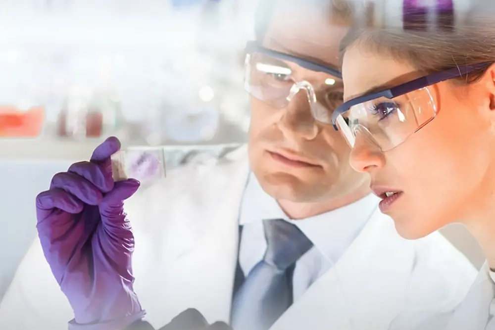 Egy nő és egy férfi arca, akik egy laboratóriumban mintát nézegetnek