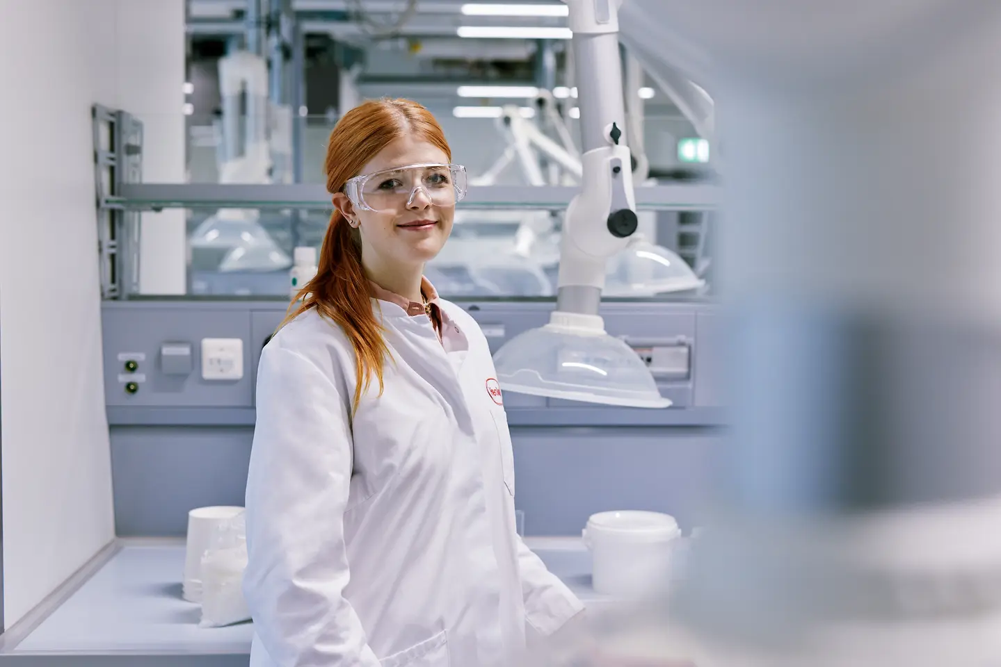 Egy frissen végzett diák, aki karrierjét a Henkelnél kezdi, fehér laboratóriumi köpenyt visel, modern laboratóriumi környezetben áll, a háttérben műszaki berendezésekkel.