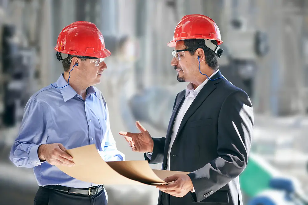 Engineers in red hard hats in a production facility.