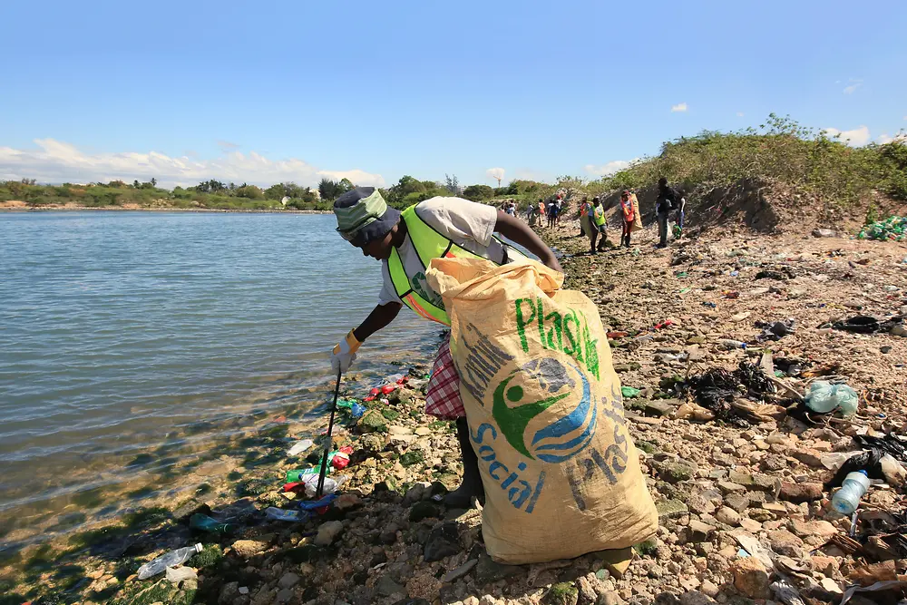 Woman collecting plastic waste on beach in Haiti